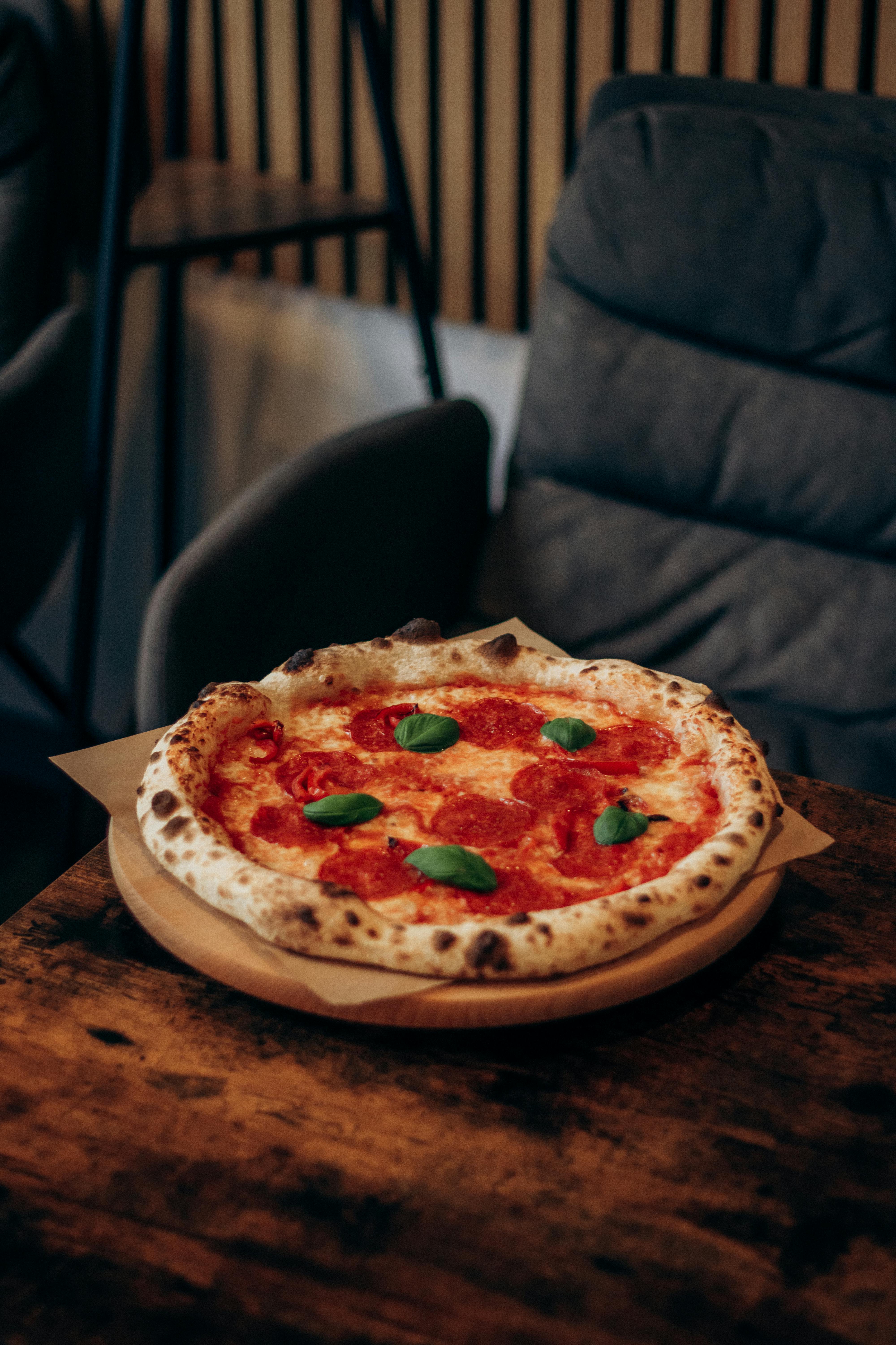 Wood-fired pepperoni pizza topped with fresh basil in a cozy indoor cafe setting.
