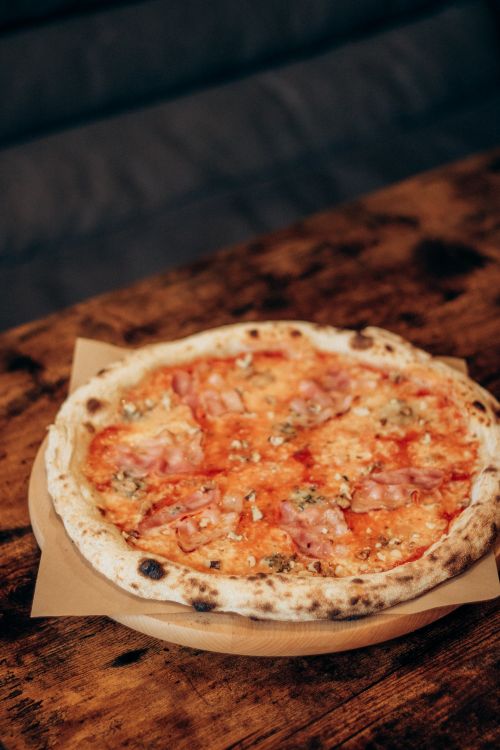 Free Mouth-watering Neapolitan pizza with ham and cheese on a wooden table setting. Stock Photo