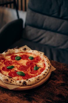 Tasty pepperoni pizza with fresh basil on a wooden table, perfect for Italian food enthusiasts.