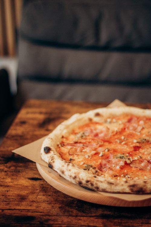 Free Close-up of a freshly baked Neapolitan pizza with ham on a rustic wooden table in a cozy setting. Stock Photo