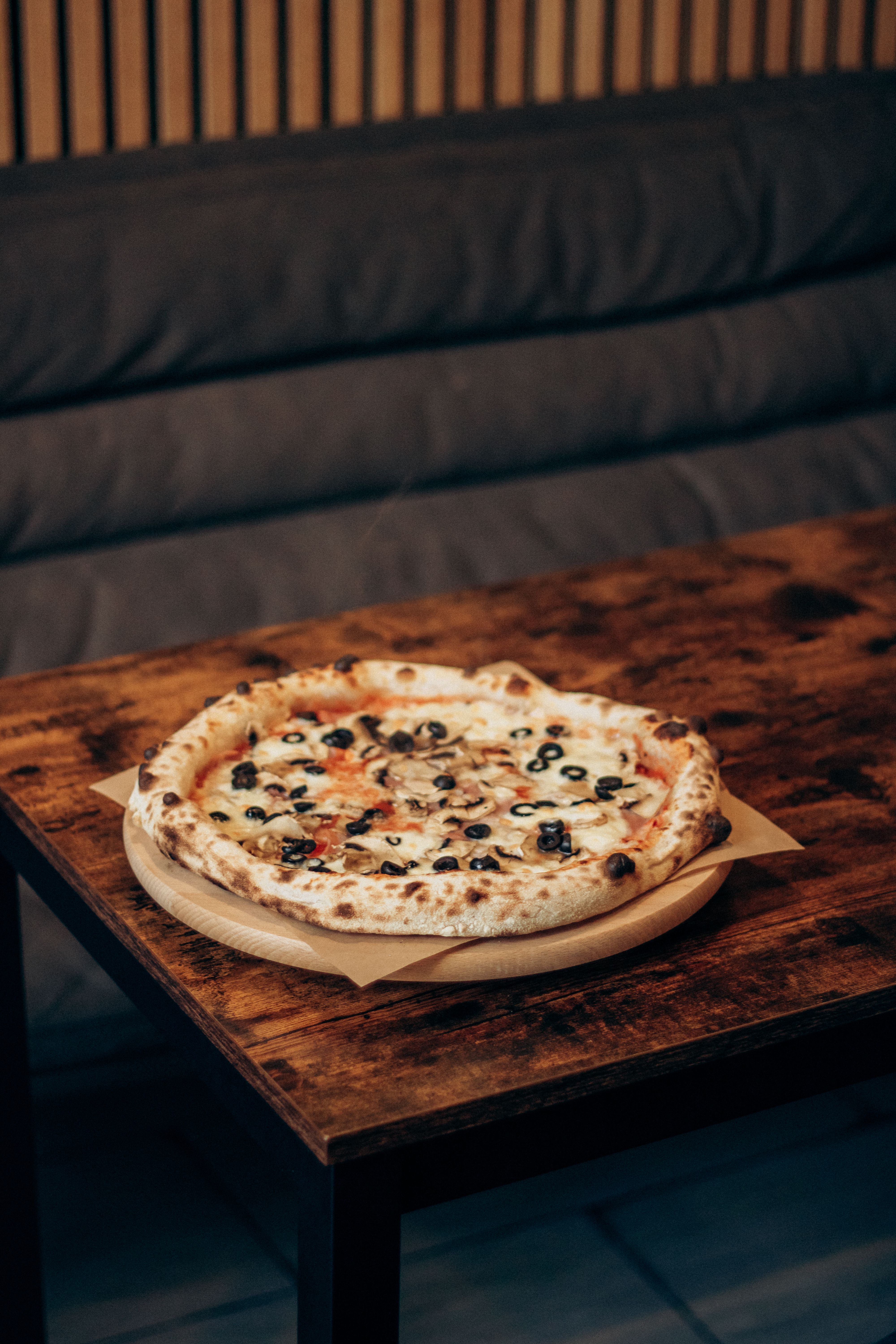 Ilmainen Suolainen italialainen pizza oliiveilla ja sienillä tarjoiltuna maalaismaisella pöydällä viihtyisässä sisätiloissa. Kuvapankkikuva