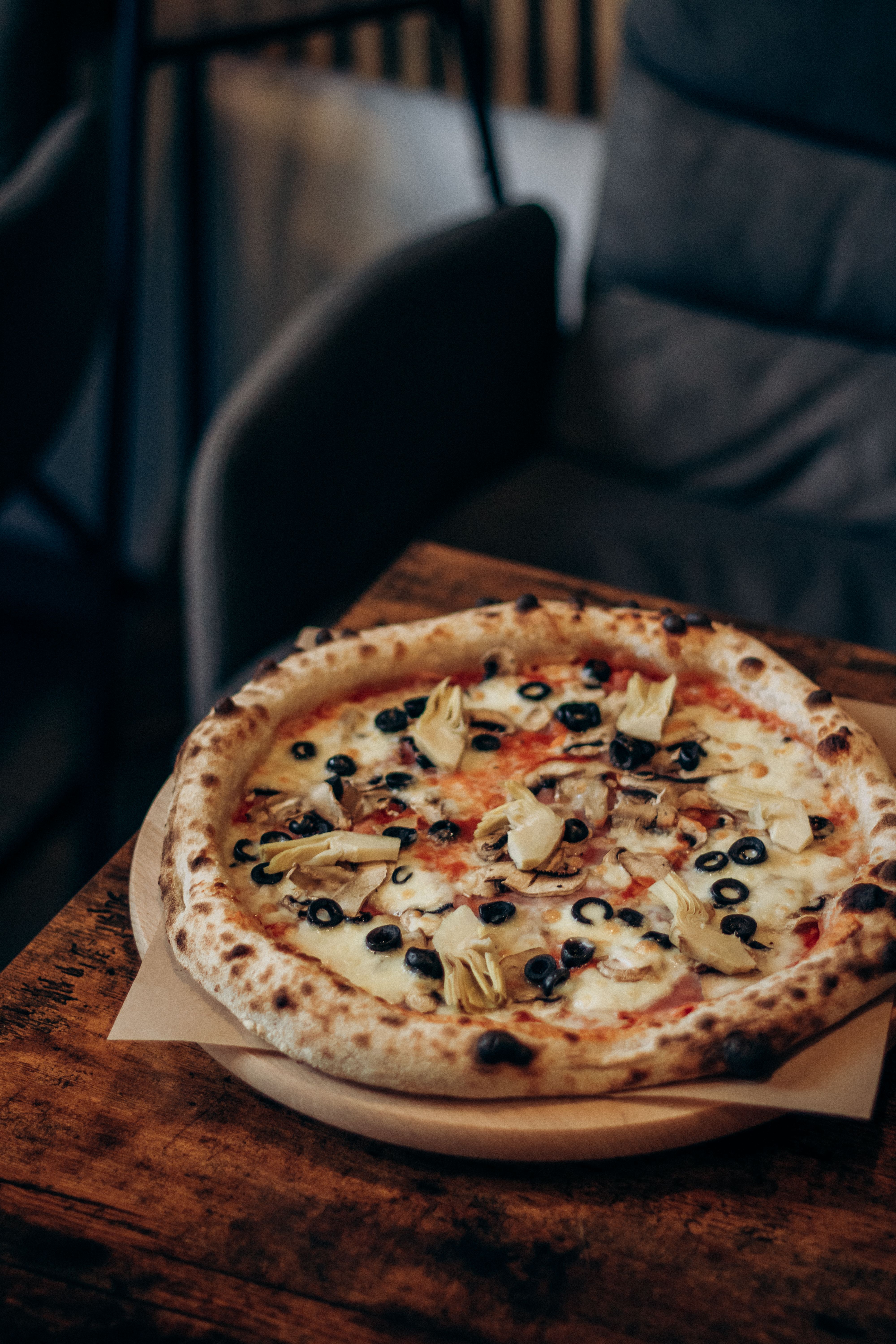 Artisan pizza with olives and artichokes on a wooden table in a cozy cafe.