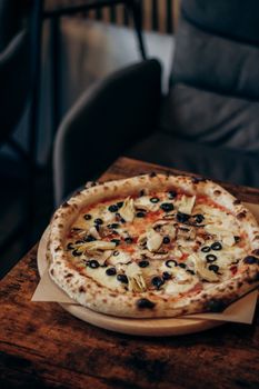 Artisan pizza with olives and artichokes on a wooden table in a cozy cafe.