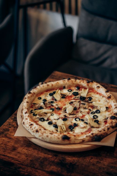 Free Artisan pizza with olives and artichokes on a wooden table in a cozy café. Stock Photo