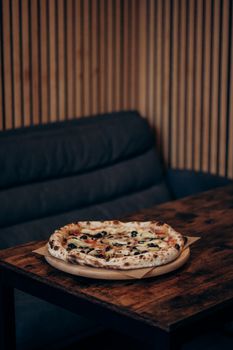 Delicious pizza with olives and tomatoes on a wooden table in a cozy indoor setting.