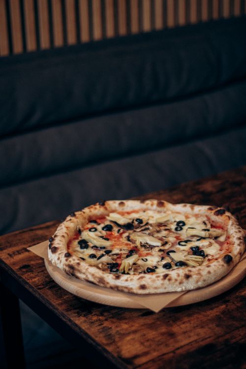 Free A tantalizing vegetarian pizza topped with fresh olives and mushrooms, served on a wooden table. Stock Photo