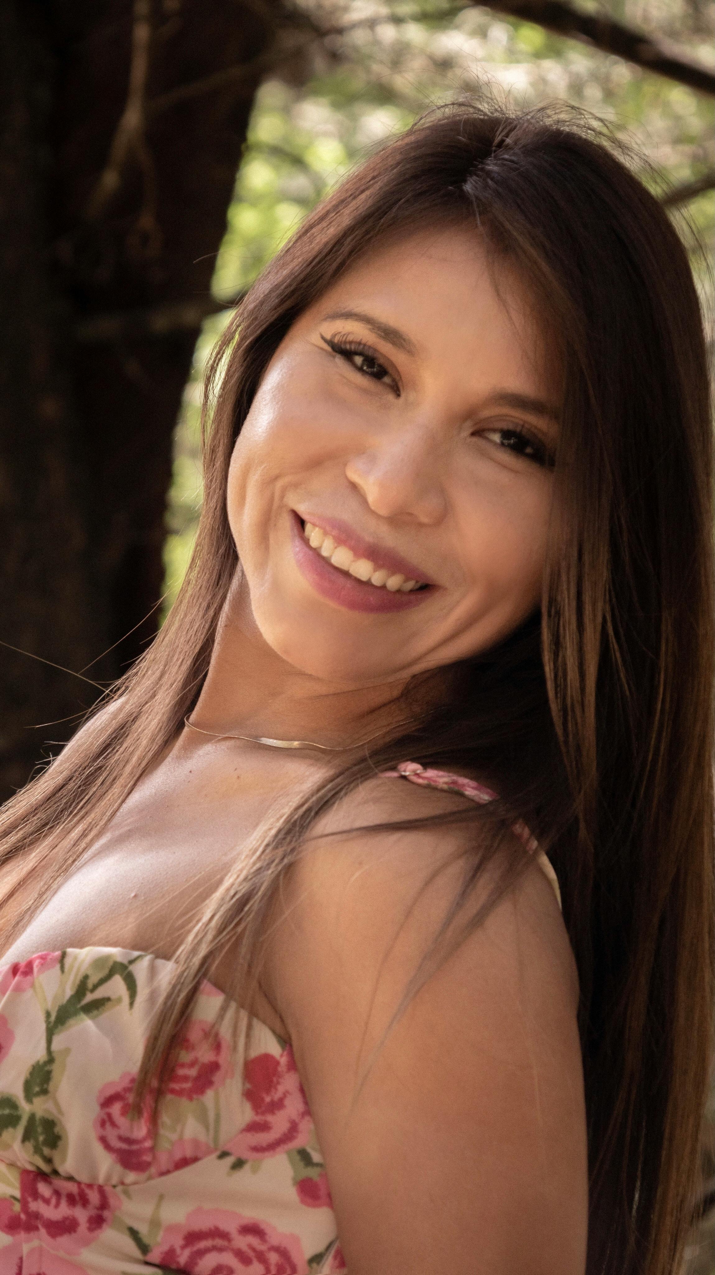 Bright portrait of a smiling woman in a floral dress outside.