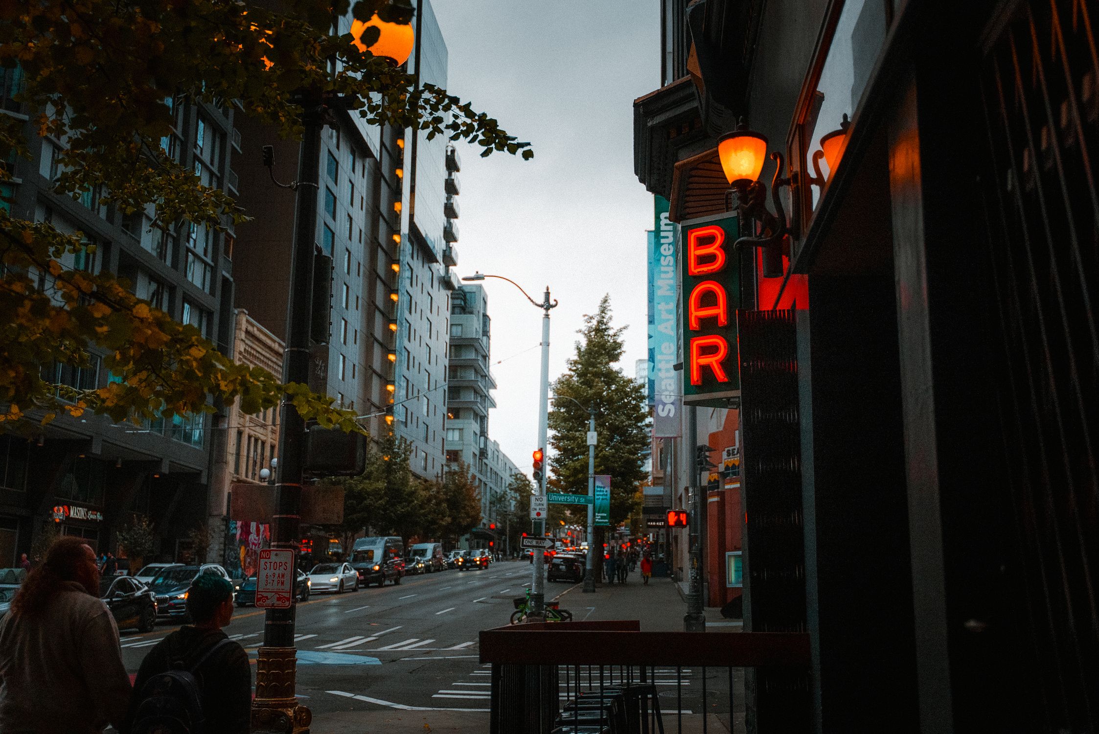 Evening view of a Seattle downtown street with a neon bar sign and cityscape.