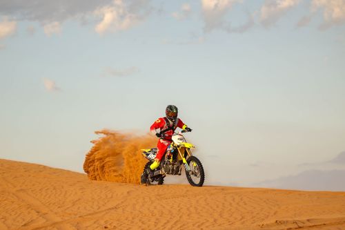 Free Motocross rider in action on sand dunes with bike kicking up sand under a clear sky. Stock Photo