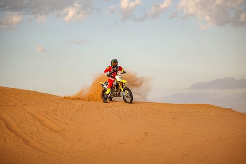 Free A motorcyclist in vibrant gear speeds across desert dunes, leaving a trail of sand. Stock Photo