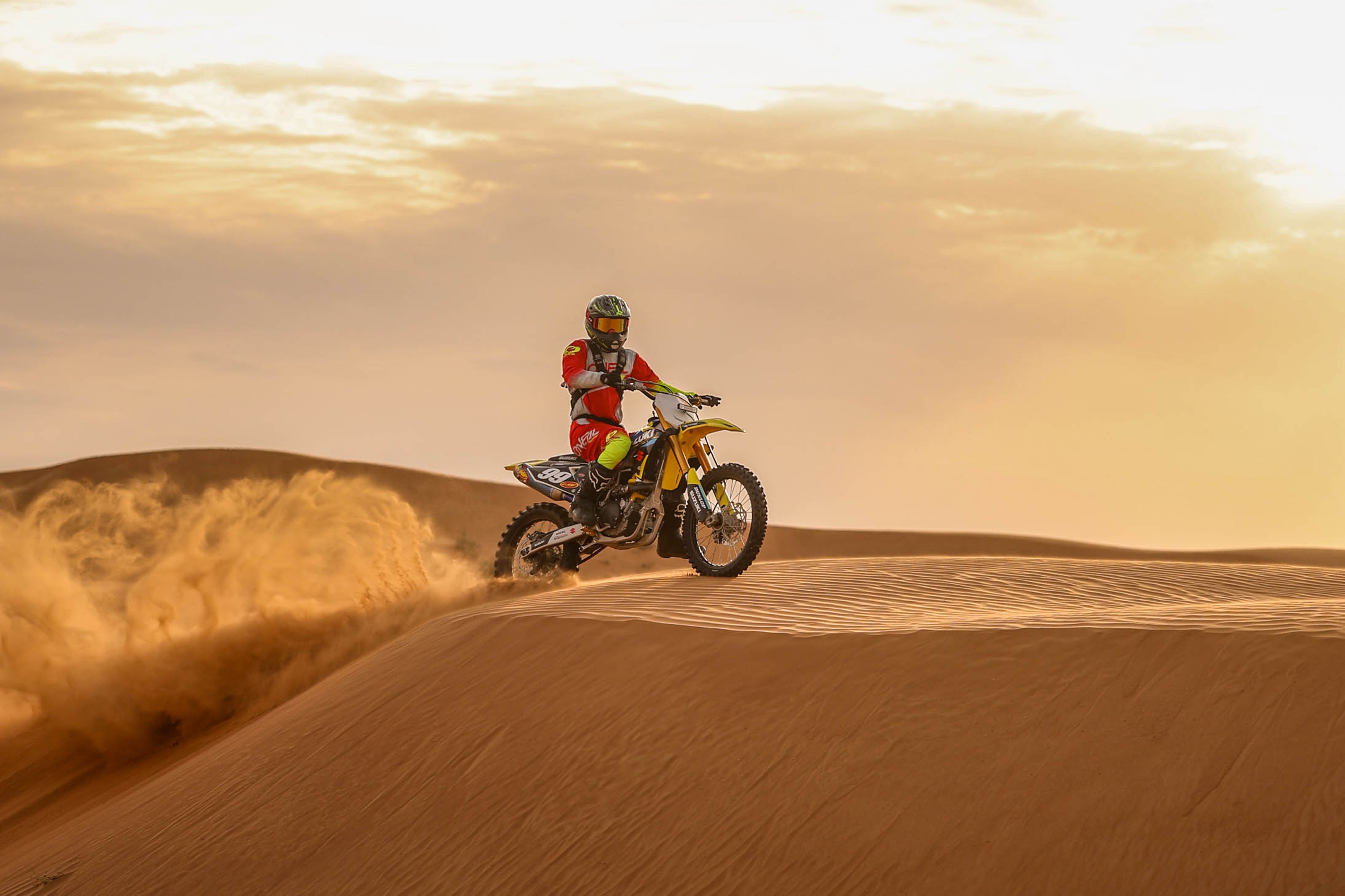 Daring motocross rider navigating sandy desert dunes in dramatic sunset light.