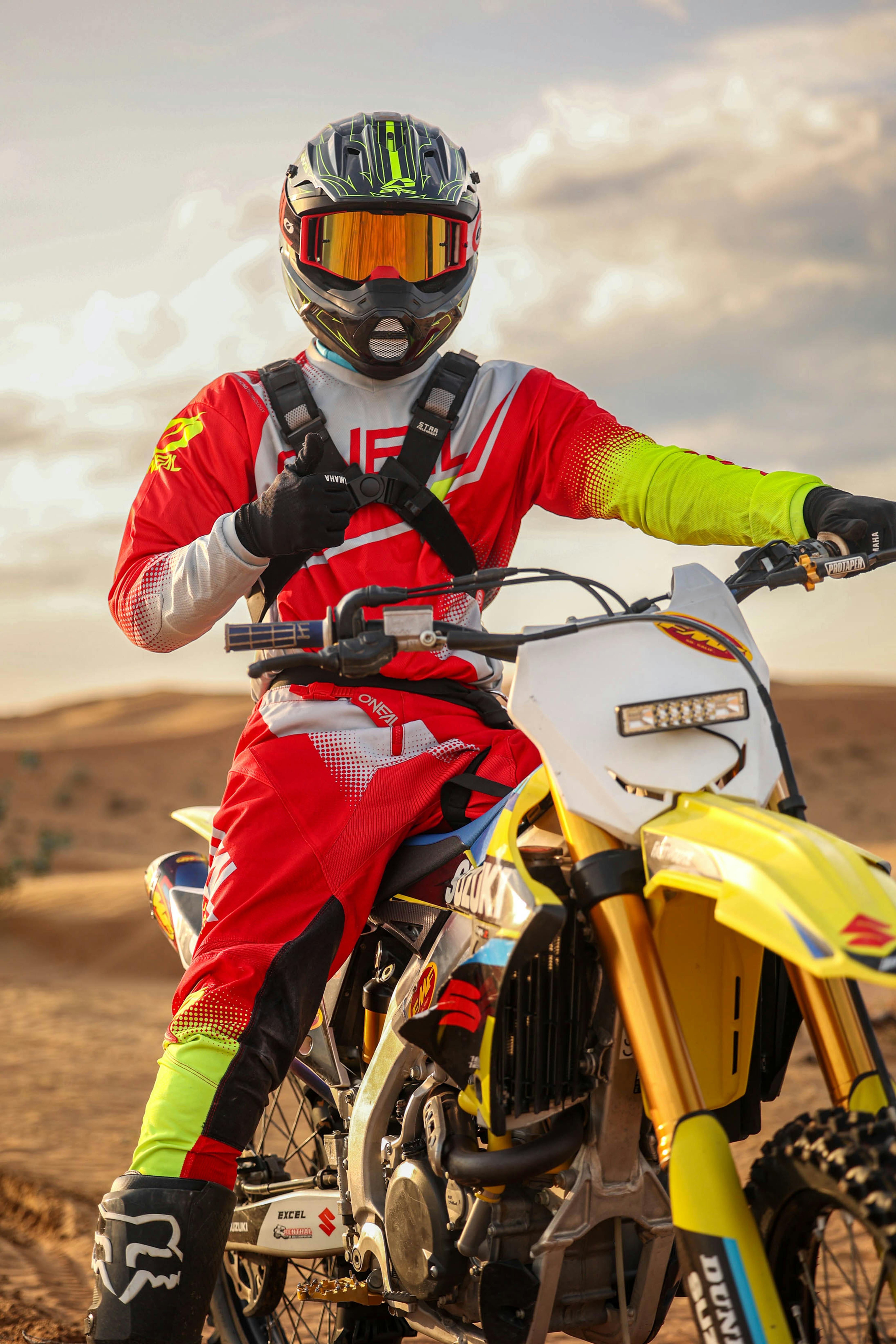 Motocross rider wearing vibrant gear poses in desert setting.