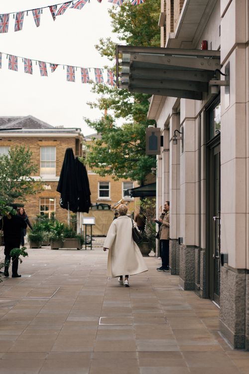 Free Elegant woman walks on London's street with Union Jack bunting overhead, city vibe. Stock Photo