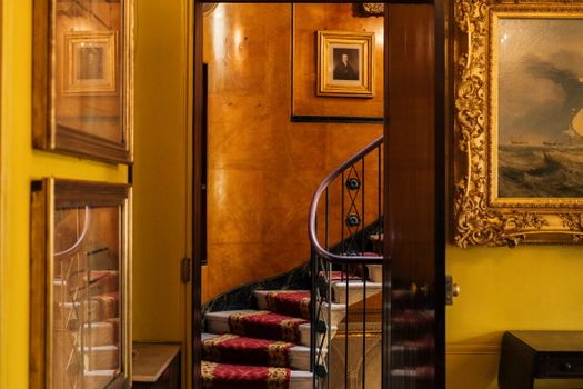 Opulent interior featuring a spiral staircase, ornate paintings, and luxurious decor in a London setting.