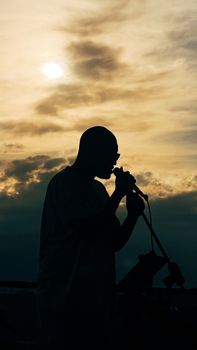 Silhouette of a singer with a microphone against a dramatic sunset sky.