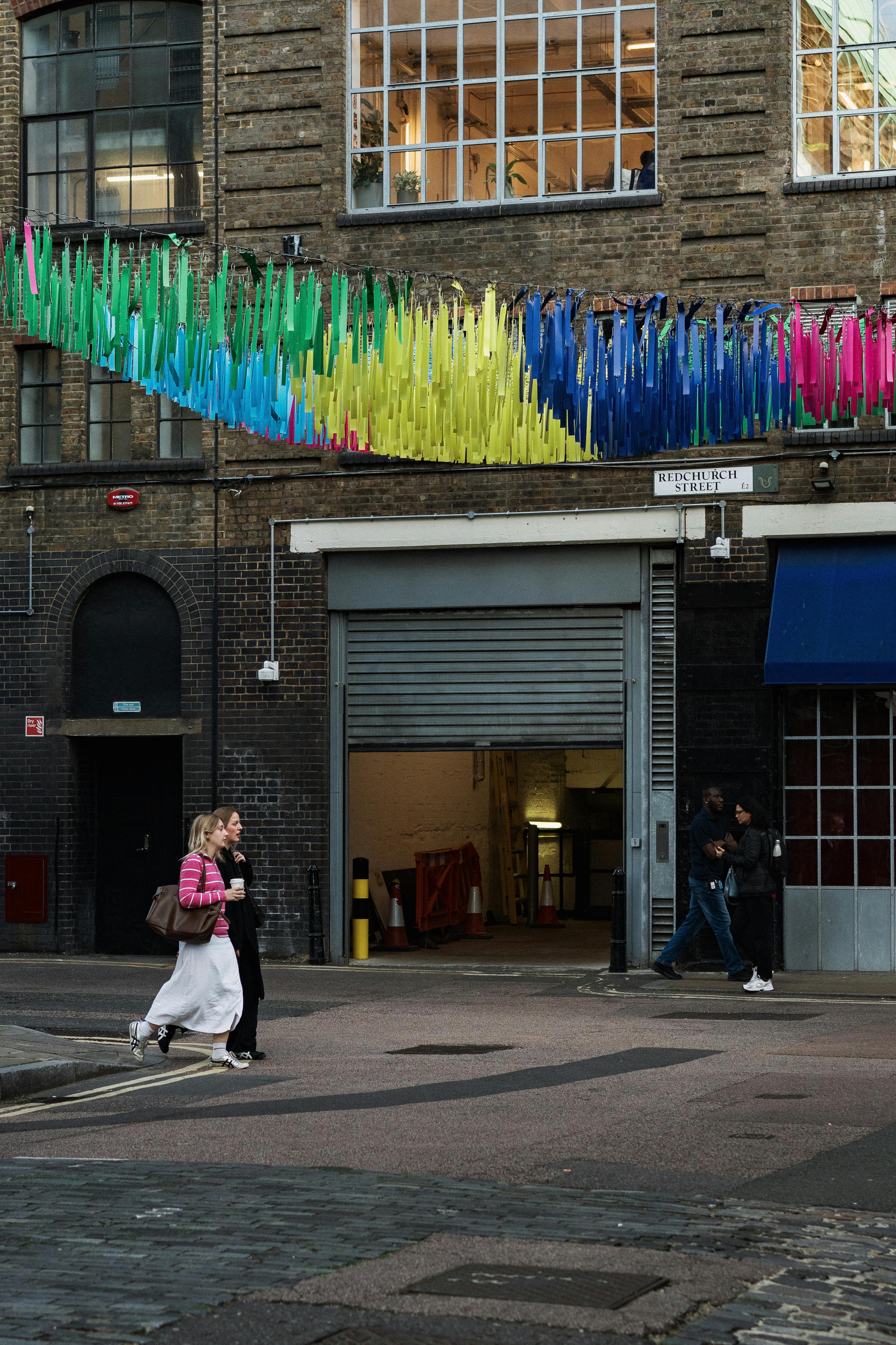 Vibrant street scene with colorful decorations in London, featuring people walking past an artistic building facade.
