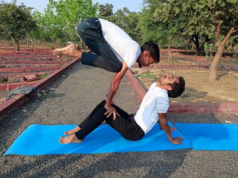 Two men performing acro yoga on a blue mat in a park in Bhopal, India.