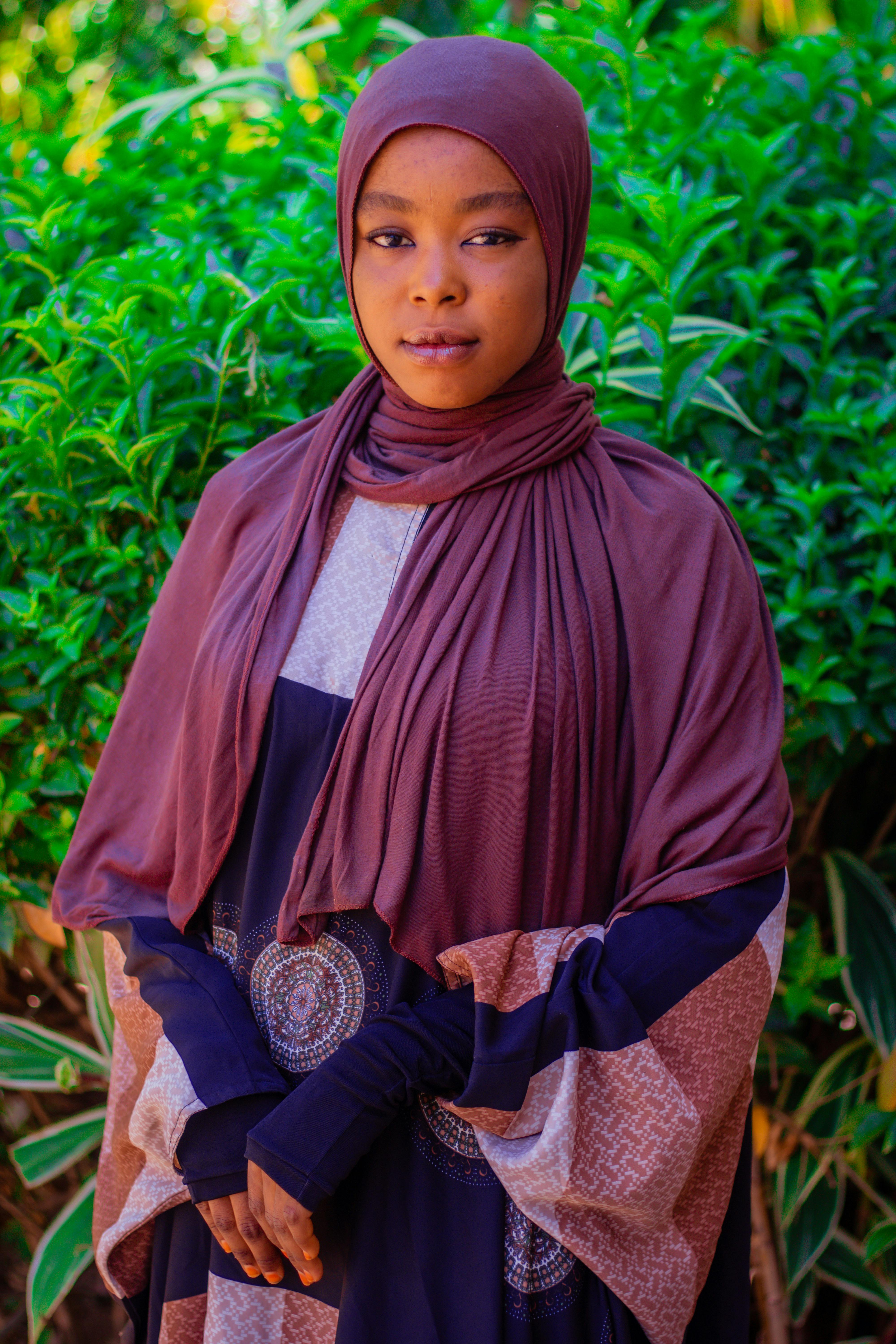 Beautiful portrait of a woman in a brown hijab against lush green foliage background.