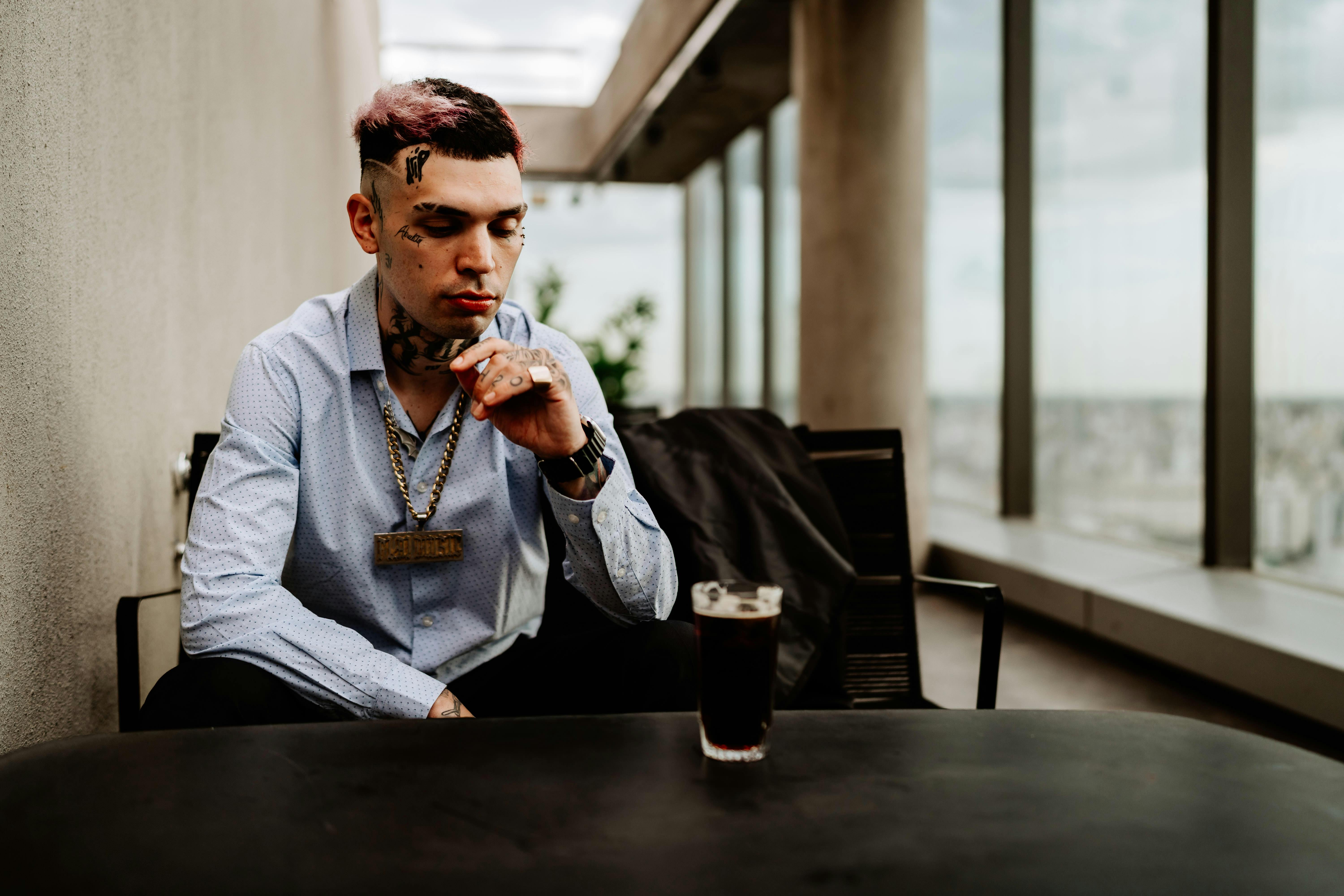 De franc Home tatuat amb una gran cadena, assegut a l'interior d'un edifici de Buenos Aires, amb una beguda a la mà. Foto d'estoc