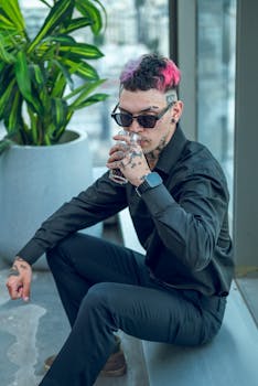 A stylish person with tattoos and sunglasses drinking indoors in Buenos Aires.