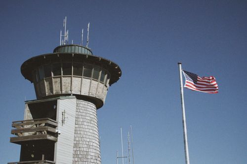 Free View of a rustic observation tower and American flag against a clear blue sky. Stock Photo