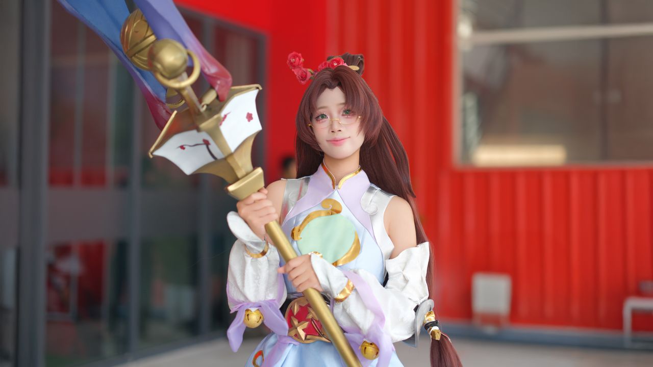 a cosplayer in a detailed costume poses with a large staff showcasing