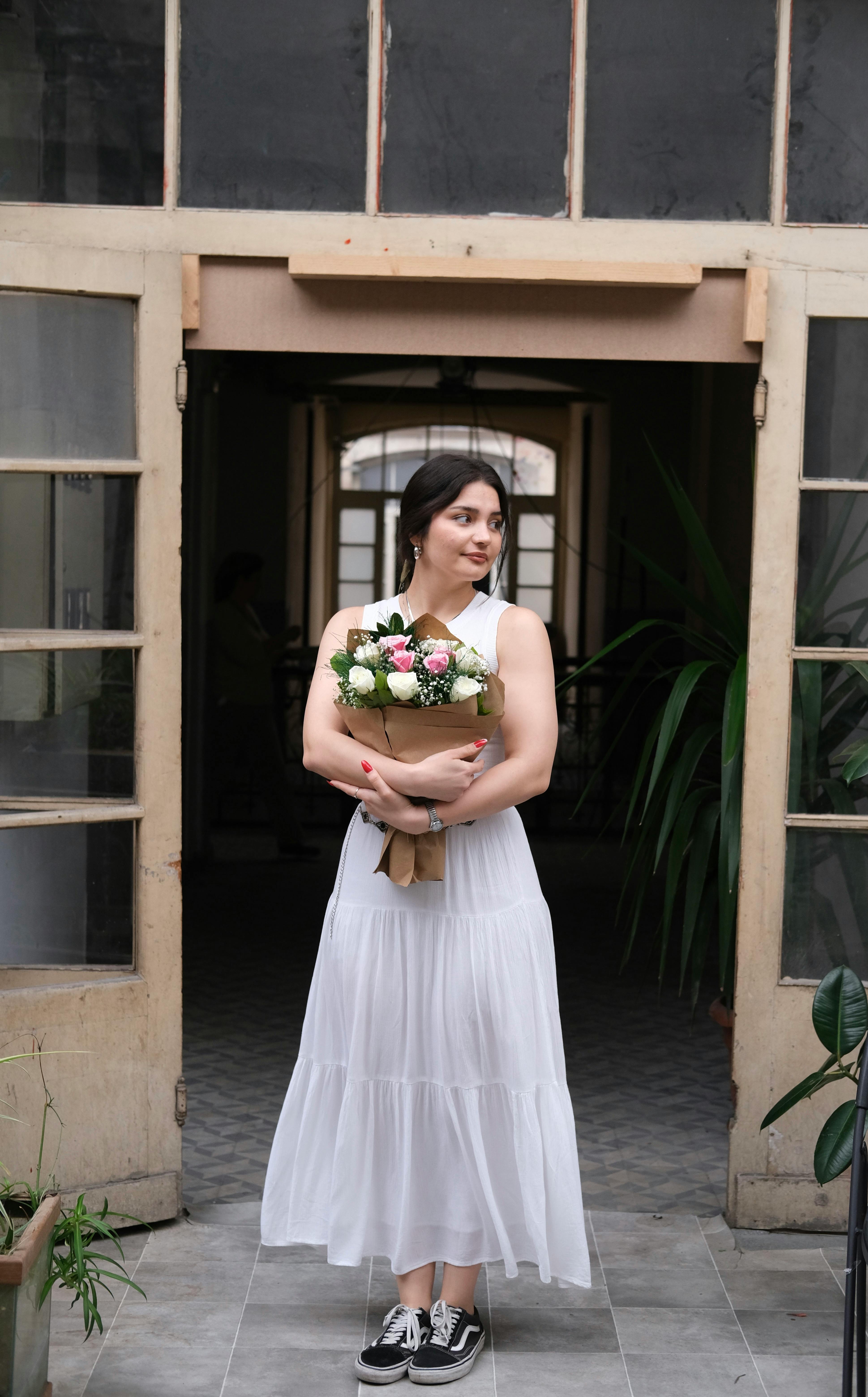 Woman in a white dress holds a floral bouquet in an İstanbul building entrance, exuding elegance.