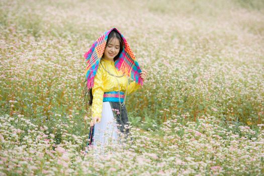 A woman in colorful traditional attire stands in a field of pink flowers, embracing nature.