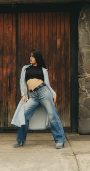 Fashionable woman in denim and black top posing confidently against rustic wooden door.