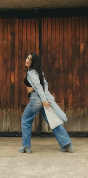 A fashionable woman in denim and heels striking a pose against a rustic wooden background.