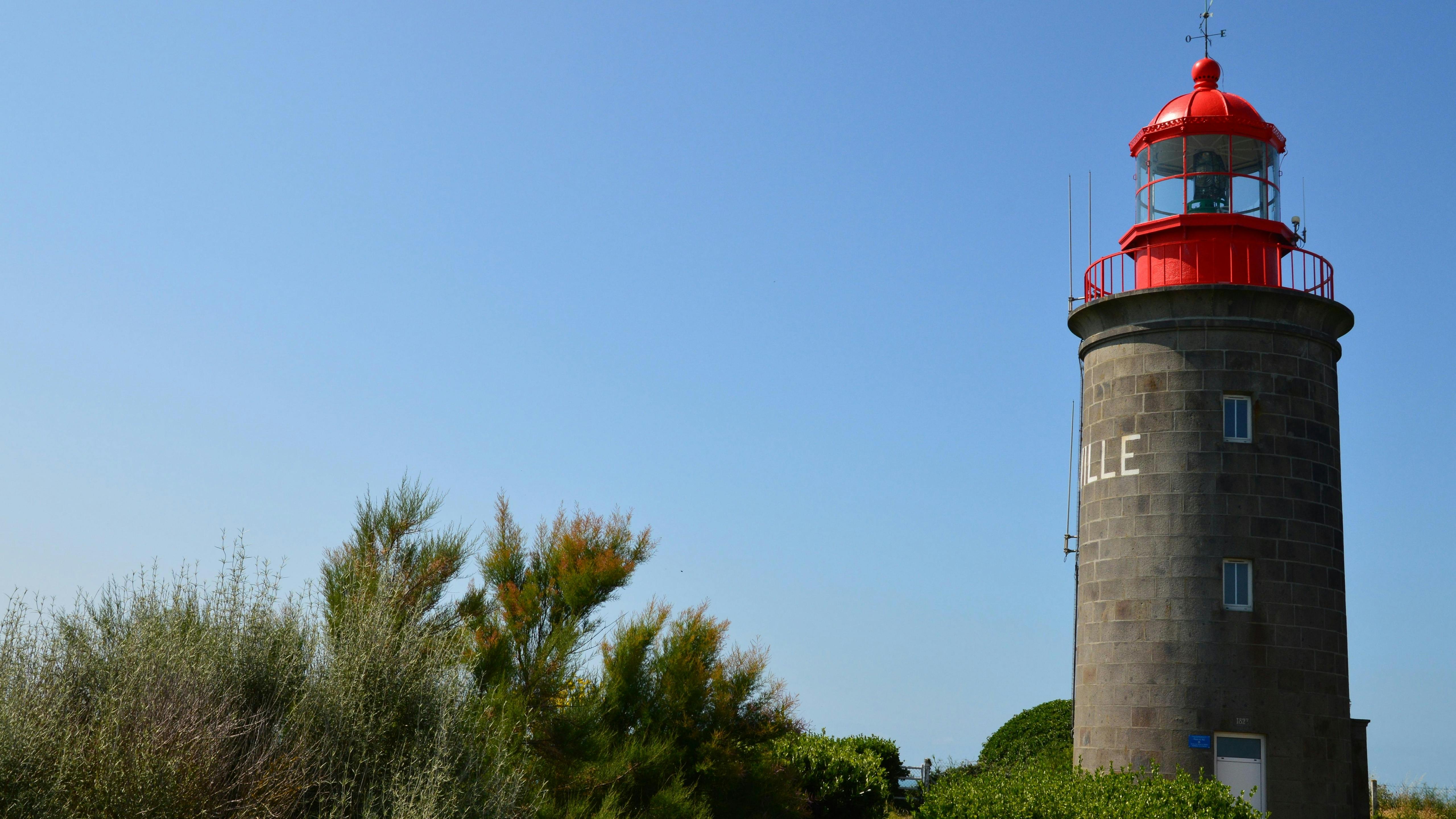A picturesque view of the Granville Lighthouse in Normandie, France against a vibrant blue sky.