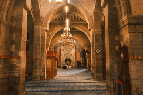 Free A stunning view of a grand mosque interior featuring a beautiful chandelier and worshippers in prayer. Stock Photo