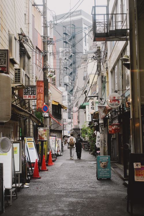 Free Busy urban alley with pedestrians, shops, and street signs in a bustling cityscape. Stock Photo