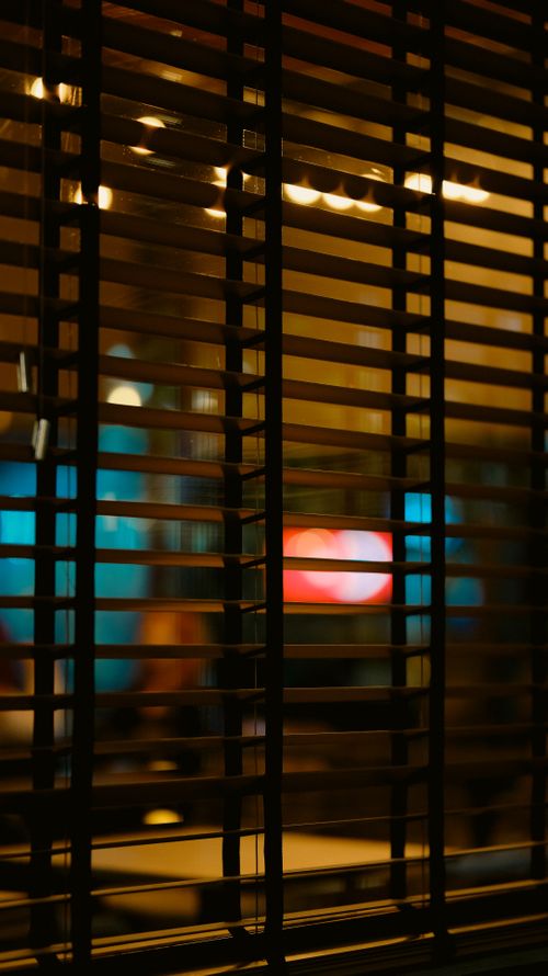 Free Atmospheric indoor view through window blinds with blurred colorful lights outside. Stock Photo
