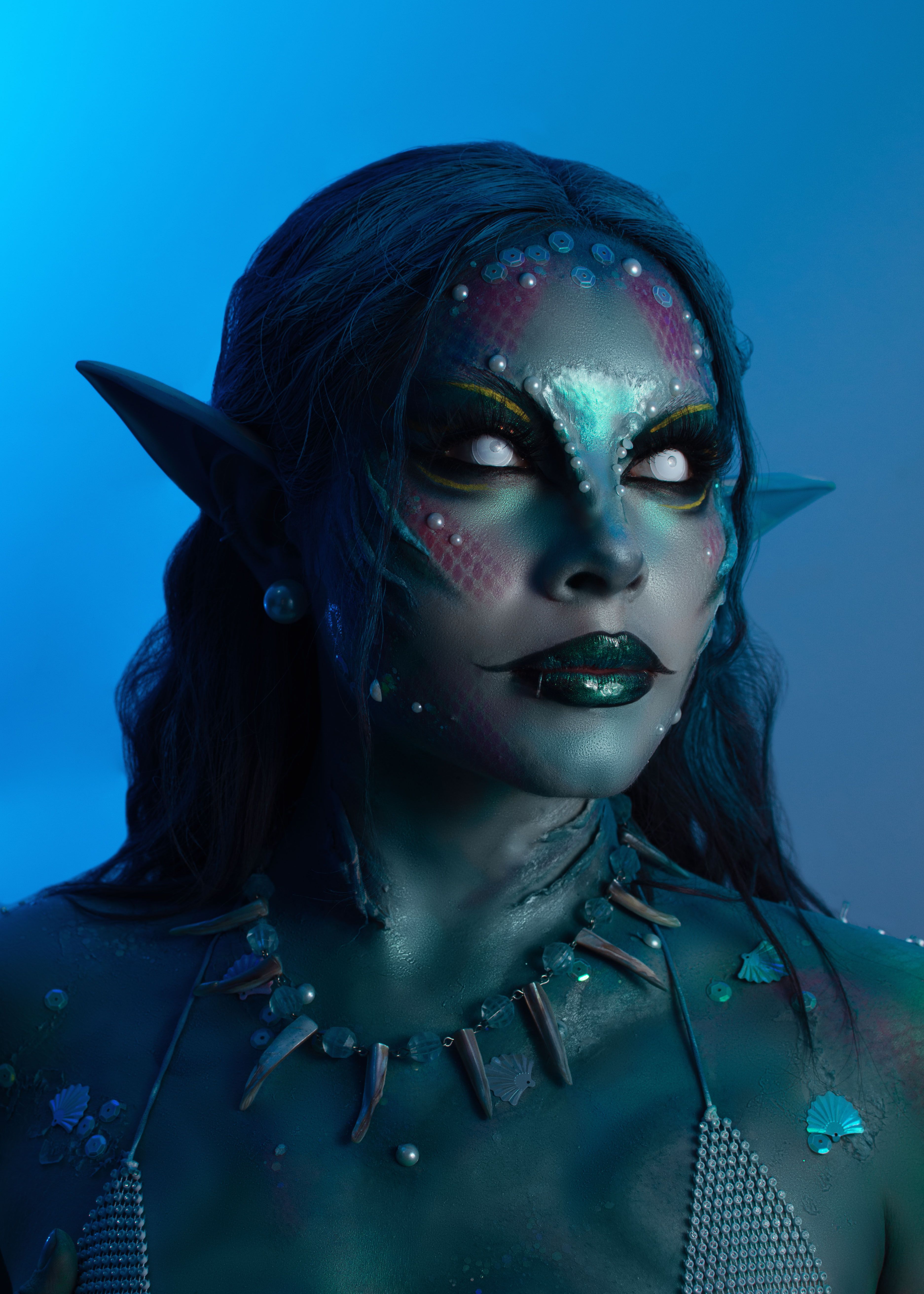 Artistic fantasy portrait of an elven character in mystical blue lighting, highlighting vivid makeup and accessories.
