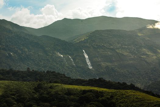 An awe-inspiring mountain landscape with cascading waterfalls and lush greenery under a bright sky.