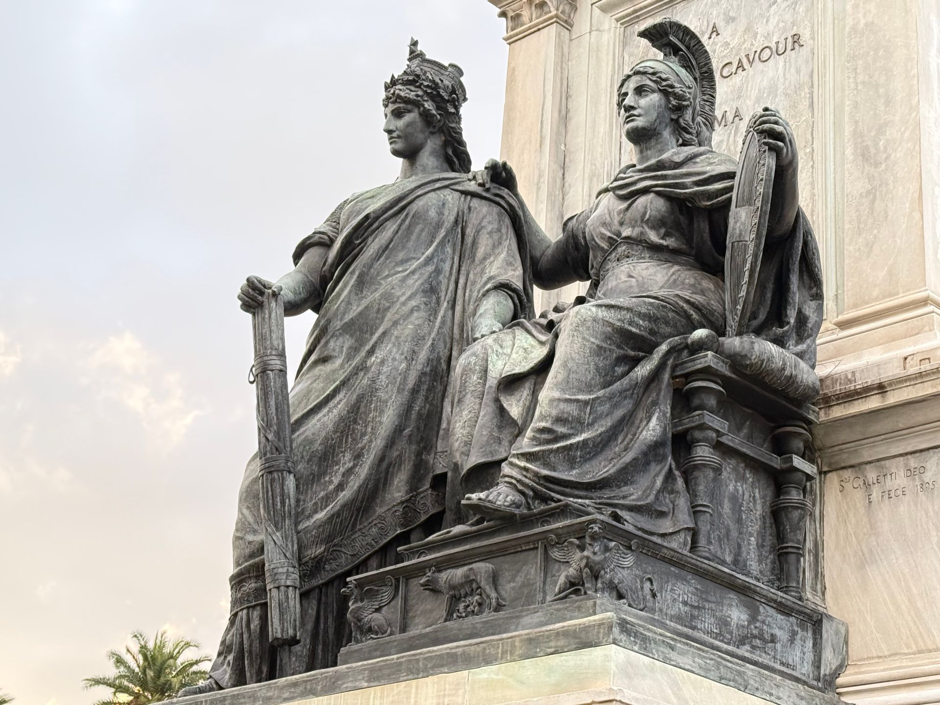 Bronze statues depicting historical figures in a European monument setting at sunset.