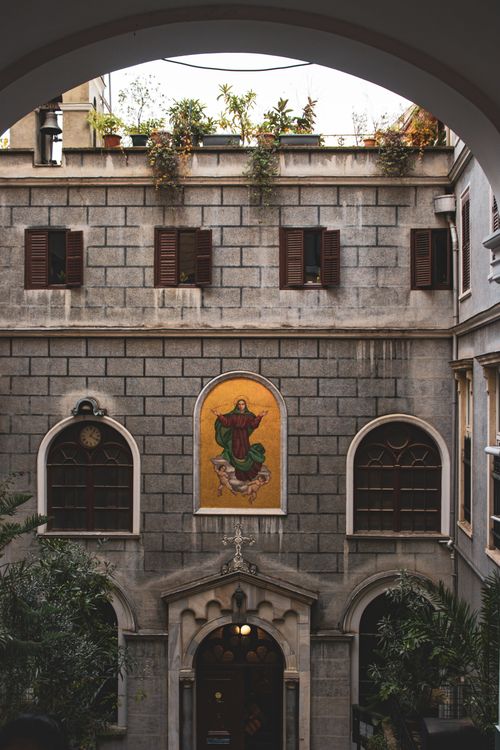 Free Vintage courtyard view featuring religious artwork on an old stone building facade. Stock Photo