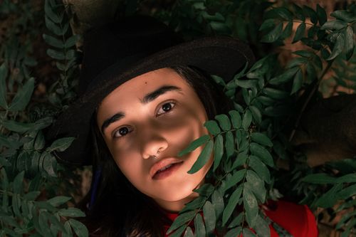 Free Artistic portrait of a woman in a fedora surrounded by greenery, highlighting natural beauty. Stock Photo