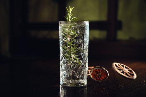 Free Refreshing cocktail served in a crystal glass with rosemary and dried citrus garnishes, perfect for elegant settings. Stock Photo