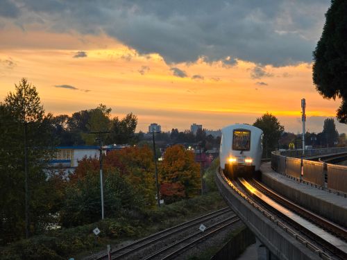 Free SkyTrain traveling under a vibrant sunset in Vancouver, highlighting the city's iconic transit system. Stock Photo