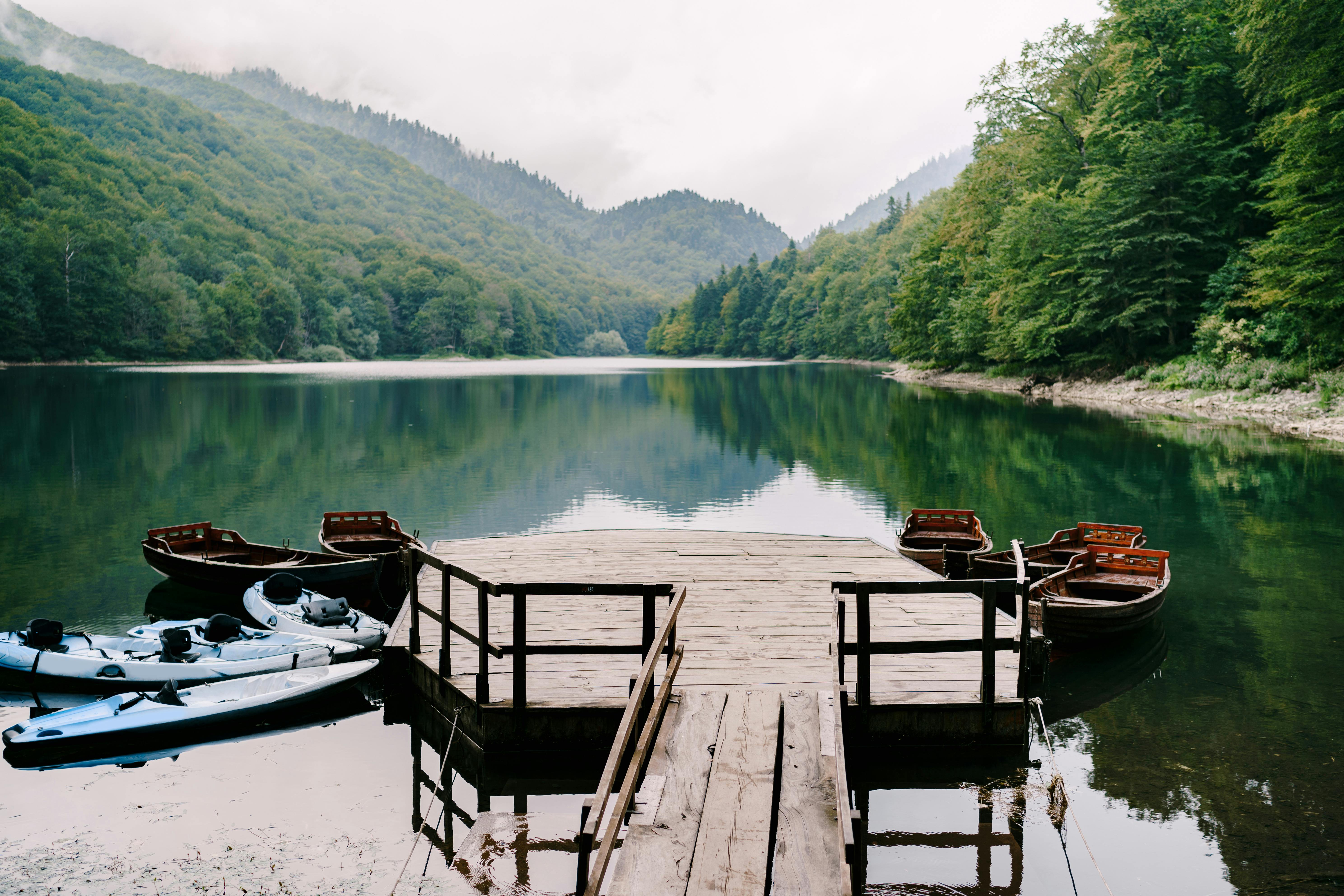 Scenic view of a peaceful mountain lake with boats and a wooden dock surrounded by lush greenery.