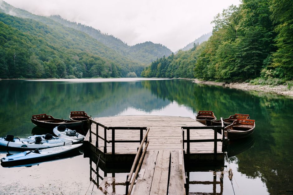 Scenic view of a peaceful mountain lake with boats and a wooden dock surrounded by lush greenery.