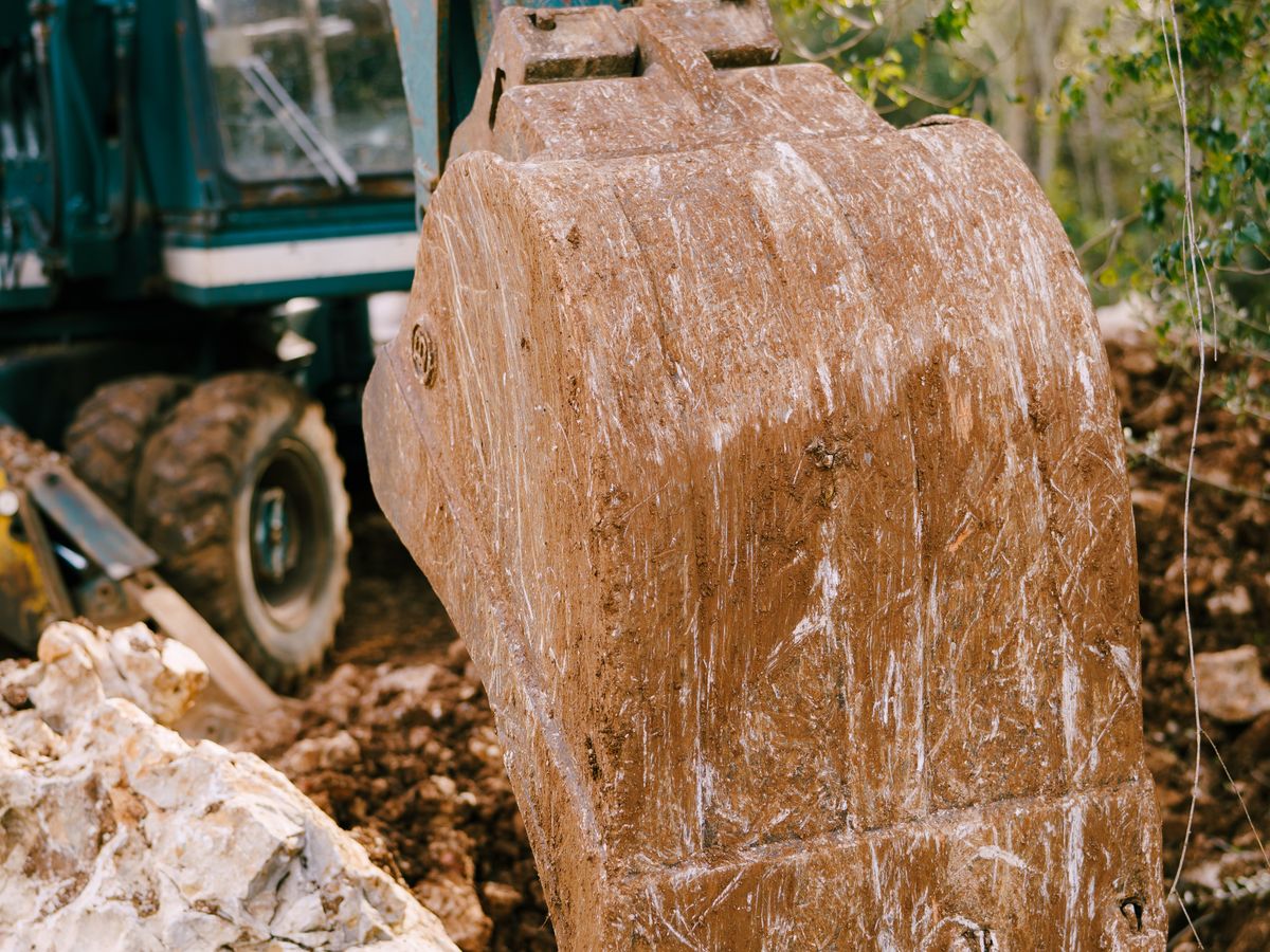 Close-up of a muddy excavator bucket surrounded by rocks and earth.