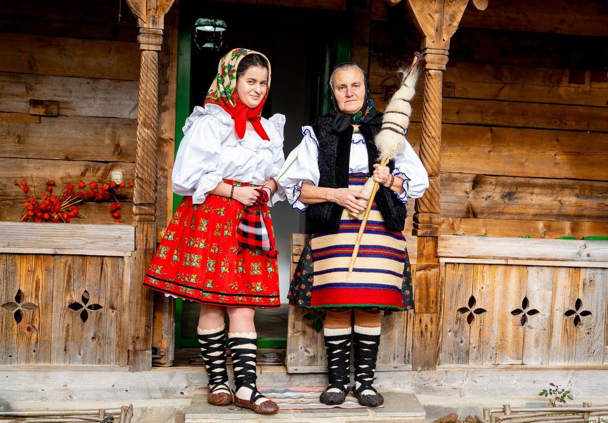 Doua femei in port popular, langa stalpi de lemn cu rozete