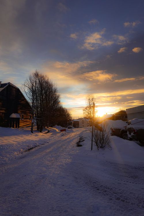 Free A serene winter evening with snow-covered streets and a vibrant sunset over suburban houses. Stock Photo