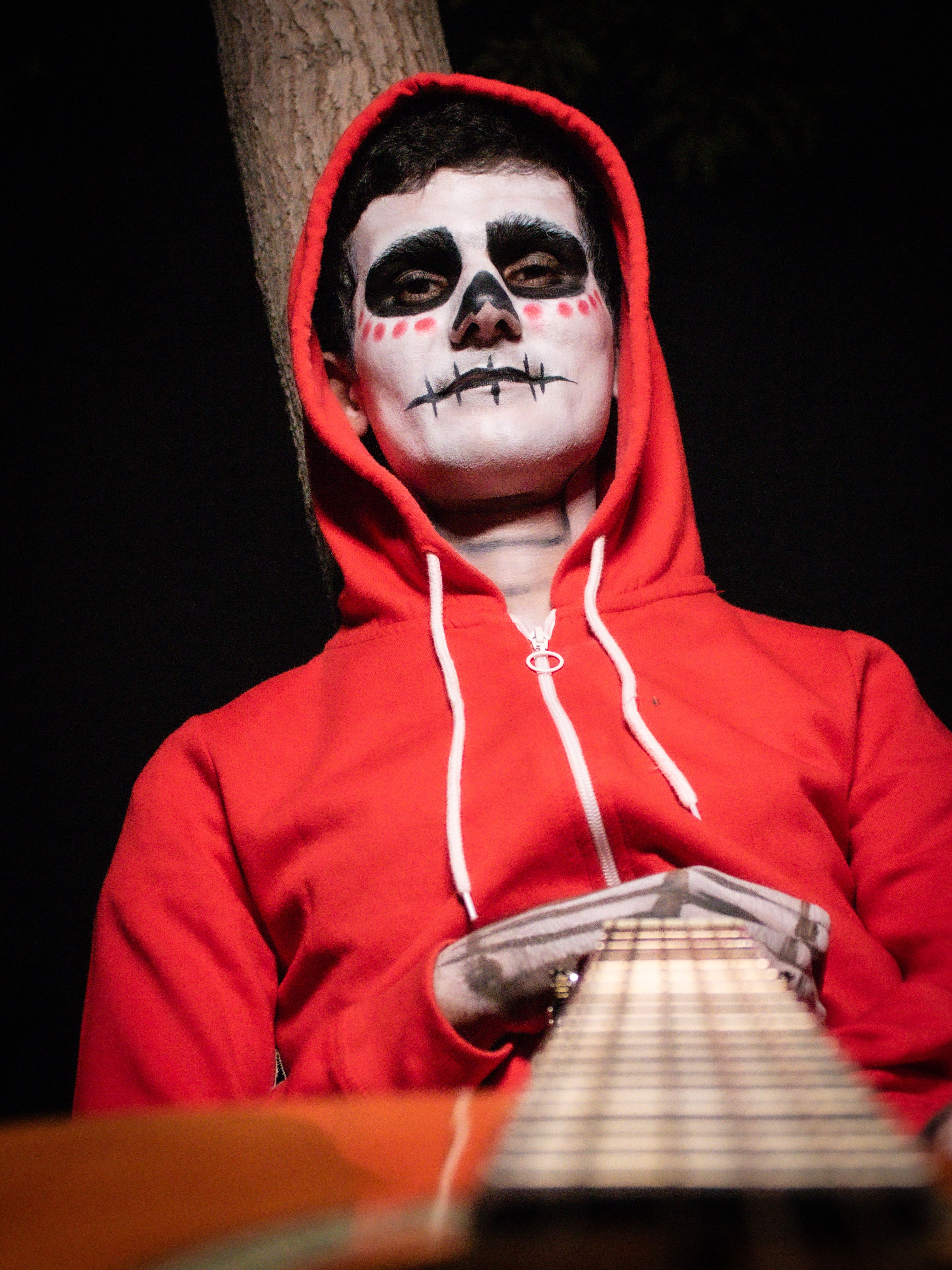 Person in Día de los Muertos makeup with red hoodie and guitar.