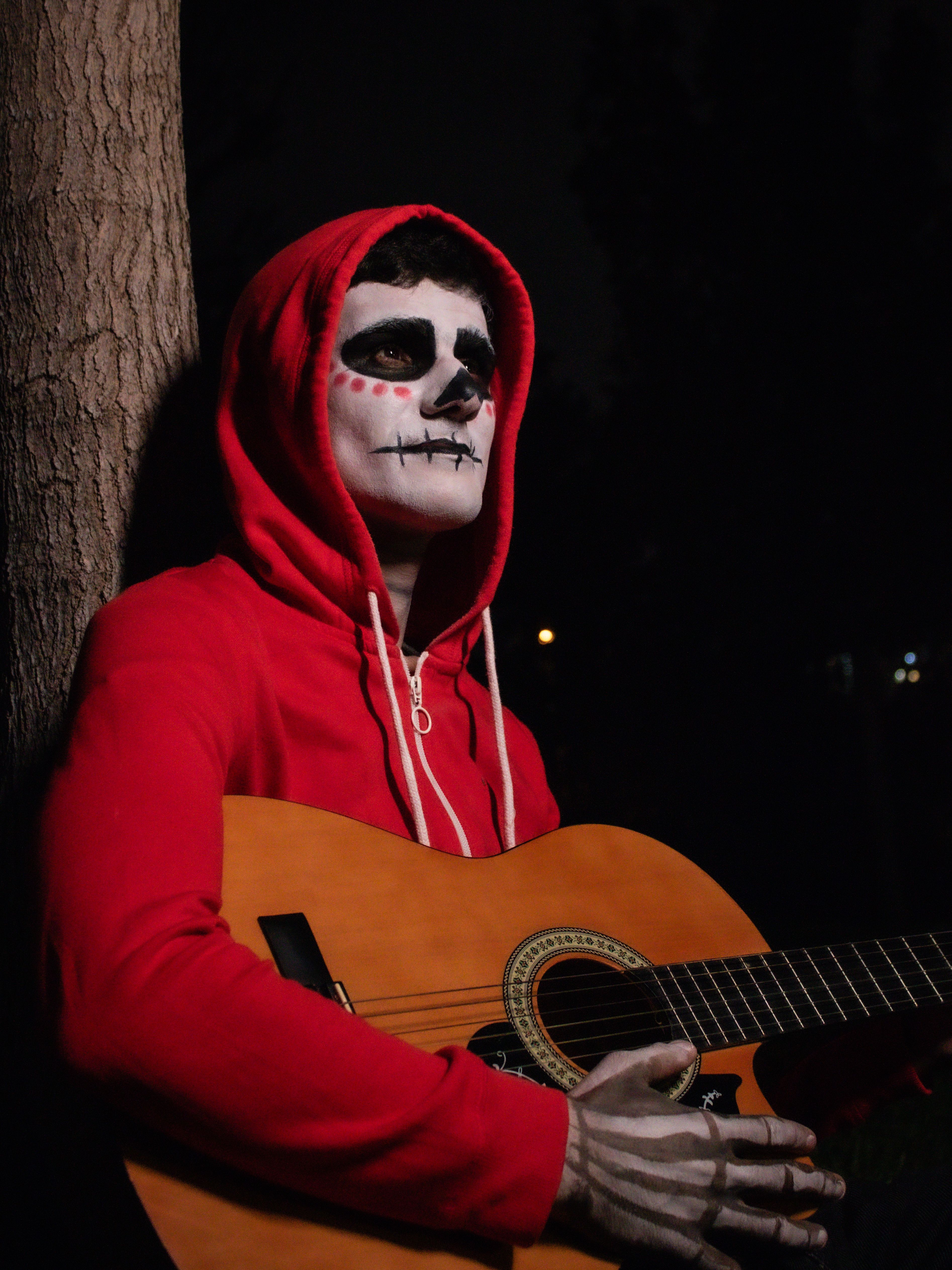 Person with skeleton makeup plays guitar at night, creating a haunting atmosphere.