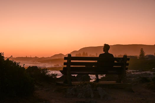 Silhouette of a person on a bench enjoying the serene sunset in Hermanus, South Africa.