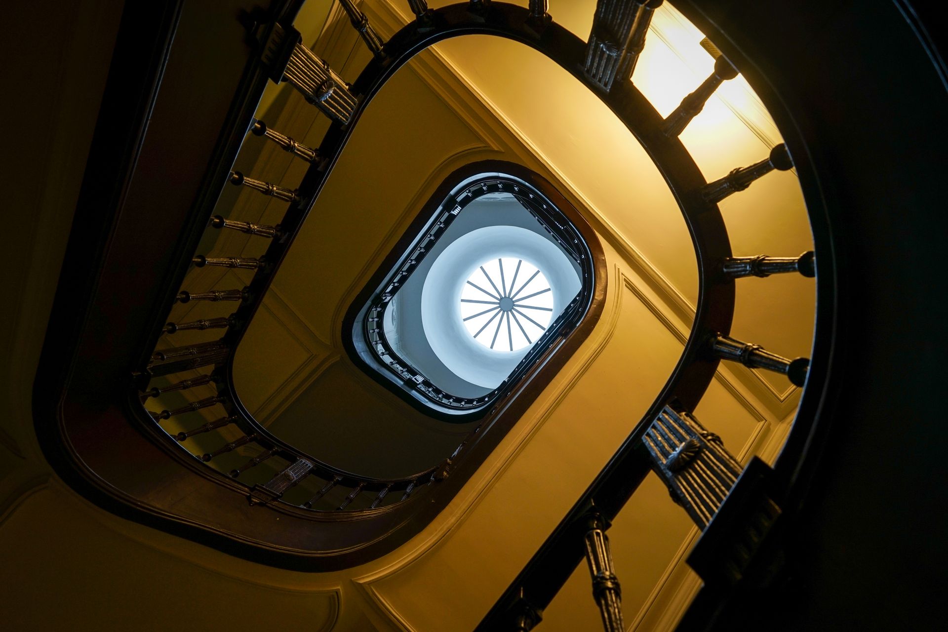 Looking up through a spiral staircase to a glowing skylight, dramatic architectural shot.